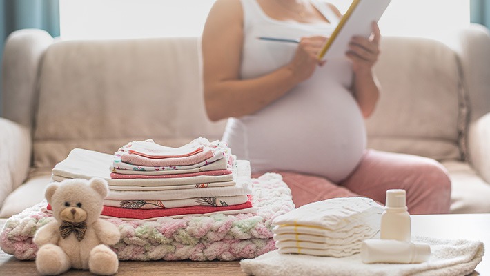 Mulher grávida segurando um bloco de notas, com itens de bebê organizados ao seu lado.